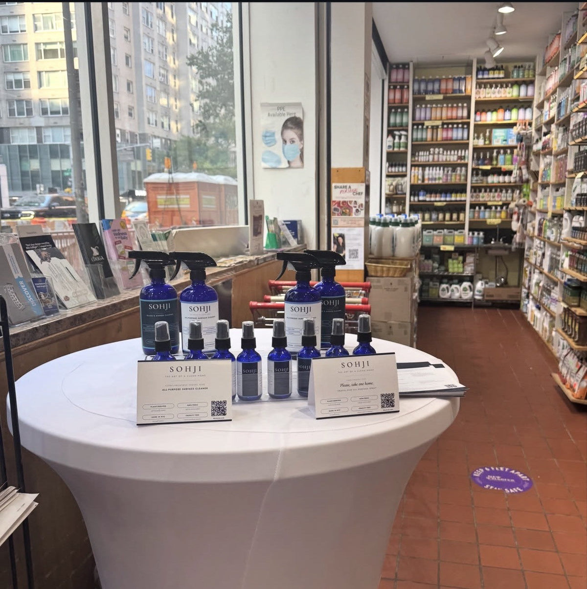 SOHJI in-store demo table with cobalt glass cleaners and travel-size samples at a NYC health food store